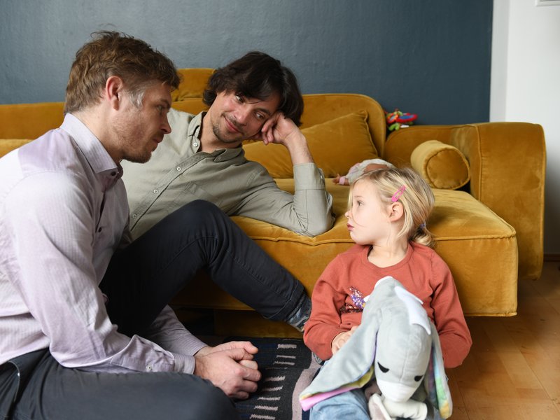 Familie vor dem Sofa Väter und Kind sitzen vor einem Sofa auf dem Boden