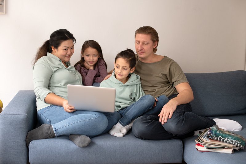 Familie mit Laptop auf der Couch Eine Familie sitzt auf einer Couch und schaut gemeinsam auf den Bildschirm eines Laptops
