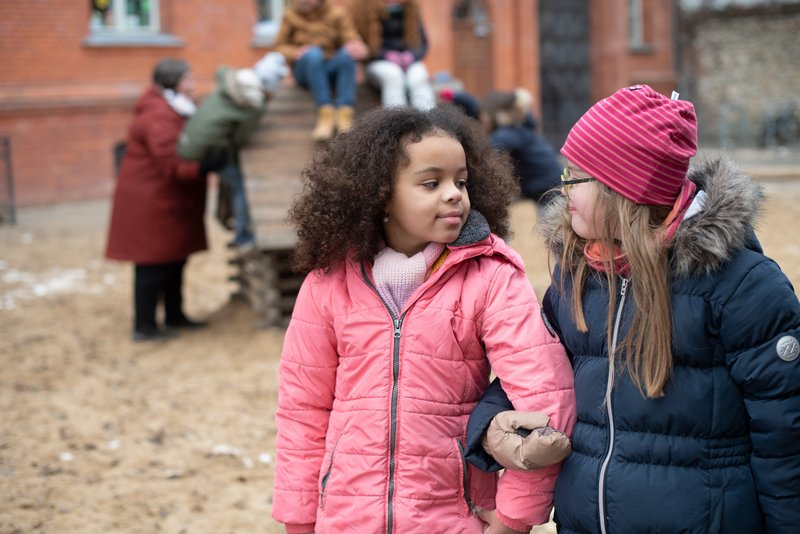 Zwei Kinder auf dem Spielplatz Zwei Kinder auf dem Spielplatz, im Hintergrund sieht man weitere Kinder und eine erwachsene Person